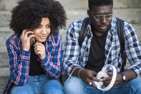 black race ethnico beautiful young couple of models and real people stay together. the girl made a phone call and the boy take a pair of headphones waiting for her. friendship and urban leisure activity conceptの写真素材