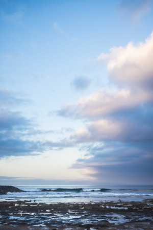 scenic landscape in early morning sunrsie for ocean rocks beach and waves for young surfers on the background. blue beautiful sky with sweet clouds. blue hours  and magic coloursの写真素材