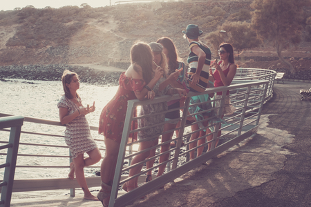 group of seven nice and beautiful caucasian girls young women have fun and laugh and smiles outdoor near the ocean during the sunset. backlight paople enjoying the outdoor leisure activity togetherの写真素材