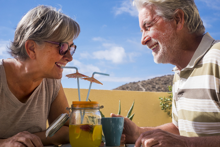 couple of adult senior in outdoor leisure activity drinking a fresh juice of fruit on the terrace together. cheerful people aged live forever. family and relationship concept for retired man and womanの写真素材