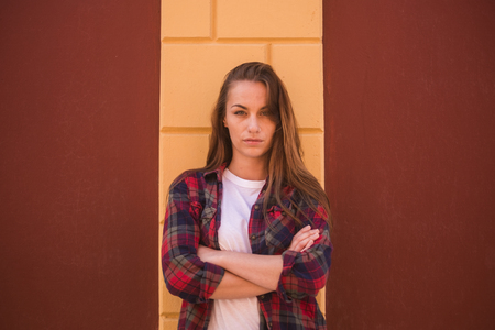 angry babe looking at you with blue eyes. red shirt hipster clothes and yellow wall on the background. beautiful bad woman with crossed armsの写真素材