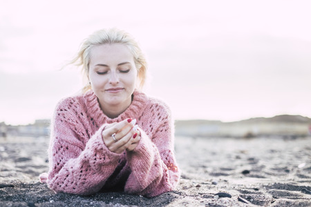 sweet attractive cheerful and thoughtful blonde yong woman lay down at the beach on the sand to enjoy the freedom and the leisure relax activity. outdoor with mountains in backgroundの写真素材
