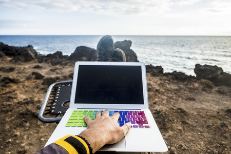 work and stay connected with internet and laptop concept. man's hand on the keyboard relaxing and working in front of the ocean. nature outdoor alternative office for traveler enjoying a free lifestyleの写真素材