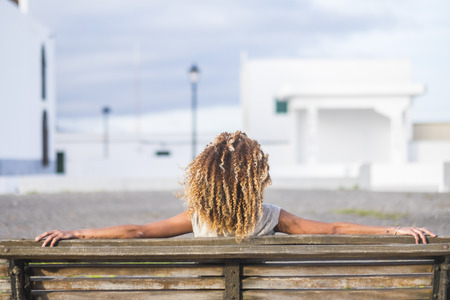 rear view of woman with curly hair sitting on the benchの写真素材