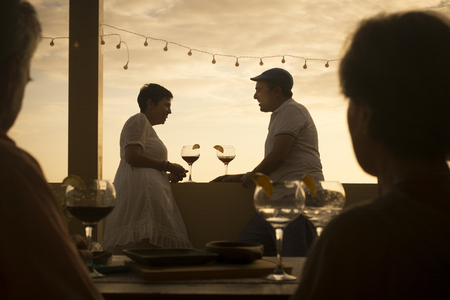 romantic scene with couple of cacuasian middle age people drinking a cocktail together in relationship during a colorful gold sunset on the terrace. having fun with romance and love vacation concept. friends in first levelの写真素材
