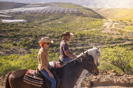 couple of rider man and woman with brown and white horses go and enjoy the outdoor leisure activity in excursion traveling the mountains. modern cowboy and no technologyの写真素材