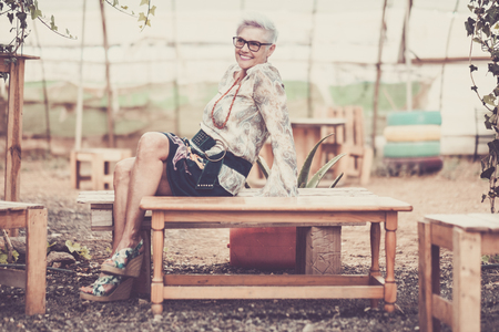 mature senior adult woman sitting and smiling on a wood recycled bench hand made build. vintage colors and hippy style mood conceptの写真素材