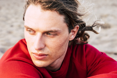 serious portrait of beautiful male model with blue eyes looking at you hidden from the arm. outdoor leisure activity for attractive male. red and colorsの写真素材