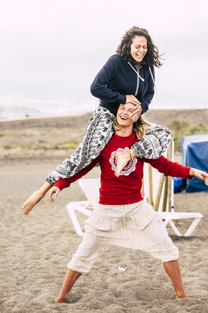 couple of caucasian young people man and female enjoy the summer beach. the man carry the female on his shoulder and both laugh like crazy while stay balanced in yoga style. happy lifestyle for travelerの写真素材