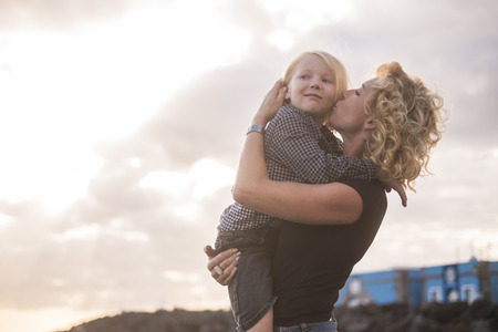 young beautiful blonde eas europe mother woman kiss her son while hug him with love and togetherness emotion and feeling. enjoy life and lifestyle for nice family outdoor - single momの写真素材