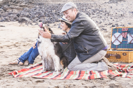 Couple in love and partnership at the beach during a picnic with best friend dog with them in playful activity. Happiness and pet therapy to enjoy life and lifestyle. Family and animals conceptの写真素材