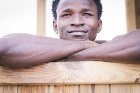 Beautiful black afro race ethnic male smile and relax on a wood bar. close up portrait of young millennial people enjoy the life and the age. Beautiness and model conceptの写真素材