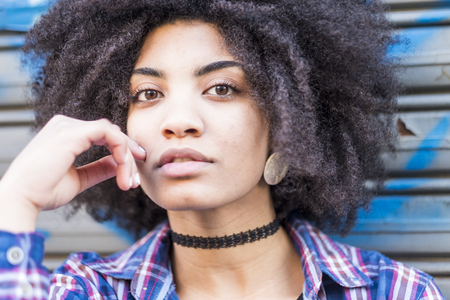 Close up portrait of a beautiful black woman smiling and looking at you. Hipster shirt and clothes for young teenager woman with attractive eyes and african hair. urban backgroundの写真素材