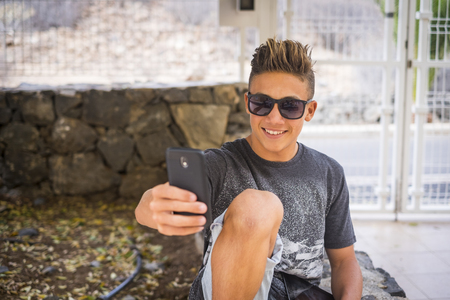 Young handsome teenager boy 15 years old take selfie picture with mobile phone smiling to the device - social media life for influencer and blogger - new work with internetの写真素材