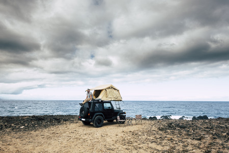 Adventure concept for caucasian man sit down and rest on the roof of his car with tent - traveler wanderlust lifestyle and different choice to live your life - feel the nature outdoor and enjoy the exploreの写真素材