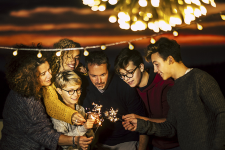 Group of friends celebrate together christmas night or new year eve or birthday or party like anniversary using sparkles light and having a lot of fun in friendship - mixed generations and families conceptの写真素材