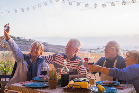 four adult matures people men and women have fun together eating and drinking on the terrace with great view on the city - the lady take a selfie picture to share the moments on social mediaの写真素材