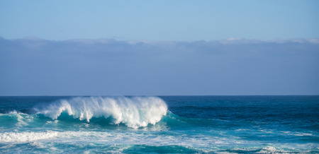 Big wave crash in the middle of the ocean with cliffs and coast in background - white splash for big swell and tide perfect for surfers - dangerous blue ocean - power energyの写真素材