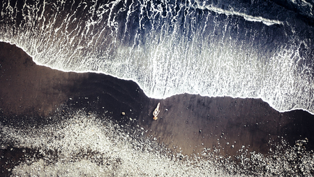 Young relaxed caucasian lady lay down at the beach on black vulcanic sand taking sun bath and waiting the big waves to dry her - vacation and travel tourist concept in top viewの写真素材