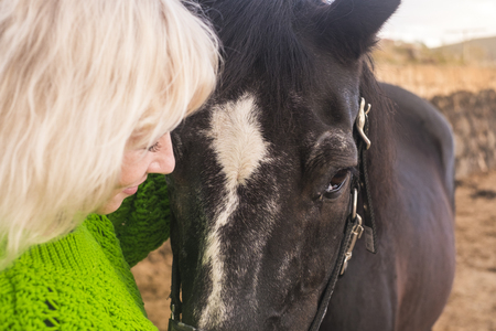 Love concept for people and animlas together in happiness and friendship. beaitufl blonde woman and dark horse in outdoor scenic place hugging and lovingの写真素材