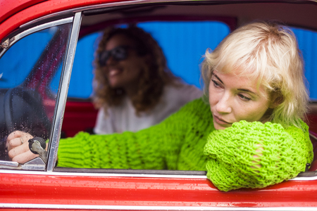 Cheerful middle age females laughing and smiling inside a red car during a rainy day while travel and move with vehicle in the city. Happiness and together friendship conceptの写真素材