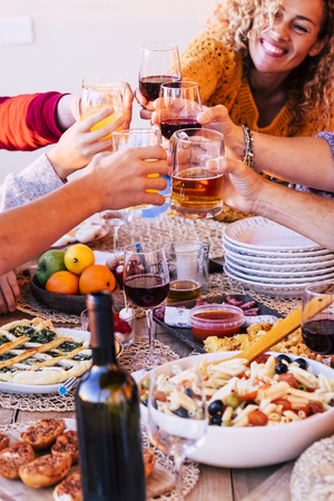 Group of friends toasting and cheering with glasses of wines and orange juice all together in friendship having fun - beautiful curly caucasian lady smiling in background - focus in the centerの写真素材