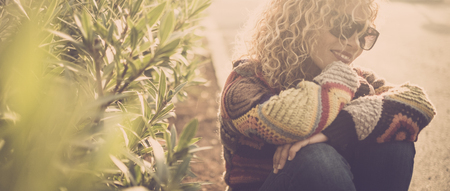 Cheerful beautiful lady sit down on the road asphalt and enjoy her lonely outdoor time thinking and smiling with her thougts and her life - vintage and sweater colors and concept for alternative lifestyle peopleの写真素材