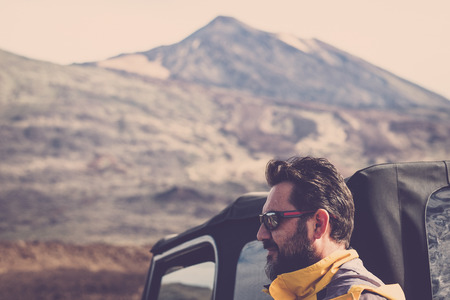 handsome middle age man with beard and sunglasses portrait. off road car and teide vulcan mountains in background for alternative vacation adventure conceptの写真素材