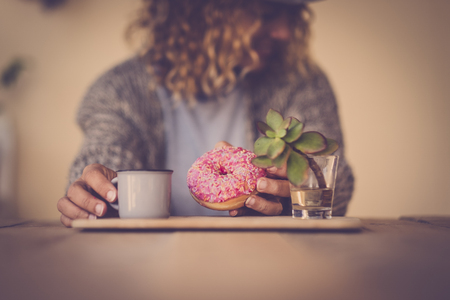 defocused portrait of beautiful woman doing breakfast in the morning at home with italian coffee espresso and donuts with pink sugar - focus on the cake - have care and diet conceptの写真素材