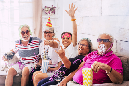 Having fun for people with no age limits at home - grandfathers and grandson all together in carnival indoor party celebration - crazy men and women with old dog pug sitting on the couchの写真素材