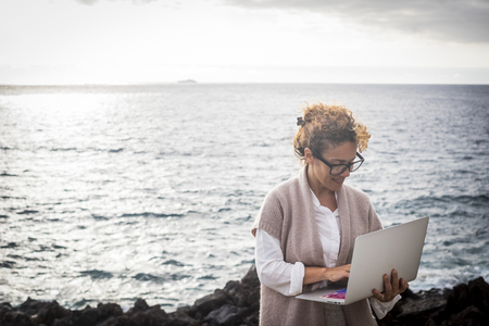 Modern woman manager work with internet and laptop everywhere without needed an usual office - alternative digital nomad lifestyle with internet and a laptop - working with ocean in background for success business conceptの写真素材