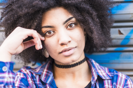 Close up portrait of a beautiful black woman smiling and looking at you. Hipster shirt and clothes for young teenager woman with attractive eyes and african hair. urban backgroundの写真素材