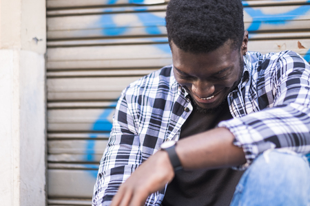 Handsome cheerful beautiful young black man african american smiling and having fun while sit and relax in the city with urban background. youthful concept for hipster style teenager boyの写真素材