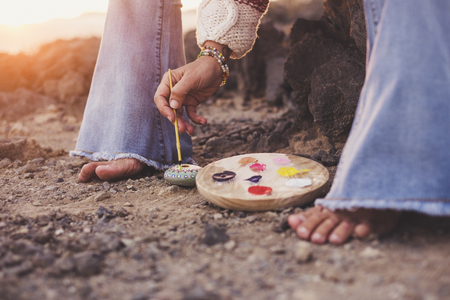 feet of woman barefoot on the ground while she paints a mandala on a stone - freeedom and oriental lifestyle concept for people love life and nature - sun in backlight during sunset timeの写真素材