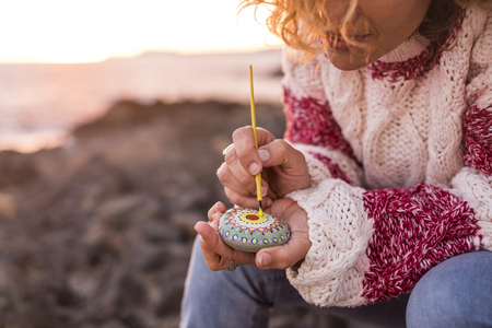 Hippy style concept female paint a mandala on a stone outdoor with sunset light in background - painting and diy hobby activity for artistic people - love and freedom conceptの写真素材