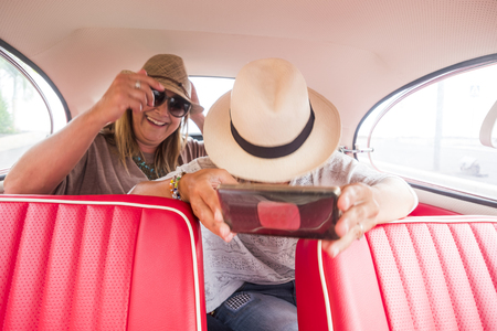 cheerful ladies caucasian and selfie with modern smart phone inside an old red vintage car. modern and old things related. internet and social networks share conceptの写真素材