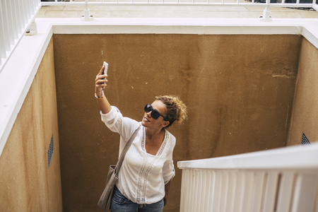 middle age caucasian beautiful lady with blonde curly hair looooking for wifi internet signal on the phone outdoor. modern people use technology and stay always connected like addictedの写真素材