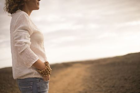 beautiful middle age lady in fashion casual clothes like jeans and white dress with big wooden bracelet standing with desert in background -の写真素材