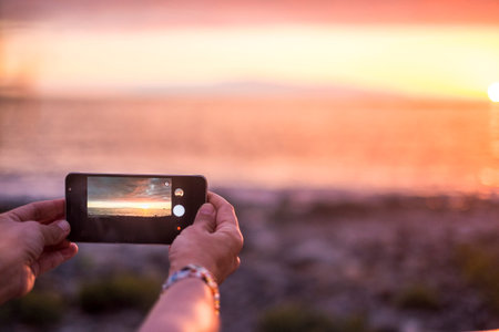 woman take picture of the sunset at the ocean in summer vacation. viewed from her smartpho0ne with...