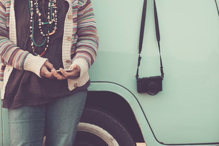 no recognizable face woman using phone technology messaging with blue vintage van in the background and retro camera on the side - travel and hippy concept imageの写真素材