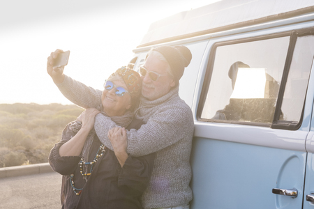 Happy old senior adult couple enjoy and have fun together with love in vacation and outdoor leisure activity using modern smart ph0ne to take picture selfie hugging and smiling with sun in backlightの写真素材