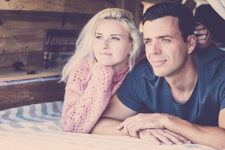 Young beautiful millennial couple looking outside laying down in a little vintage nice camper van during alternative vacation enjoying nature and travel concept - blue eyes bothの写真素材
