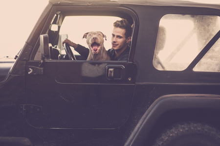Couple of crazy funny friends driving black car together: man and shouting hungry dog traveling with off road vehicle - vintage filter and brown colors for transport funny conceptの写真素材