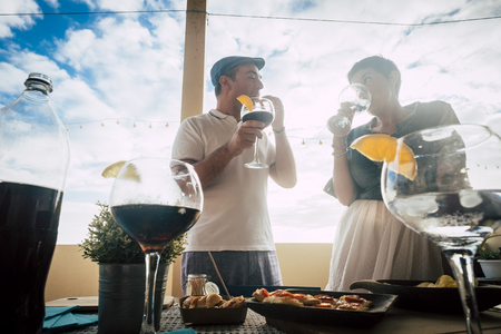 Caucasian couple enjoying celebration with cocktails and some foods outdoor at the bar or restaurant or home - first dating concept or sharing time together for middle age people - blue sky backgroundの写真素材