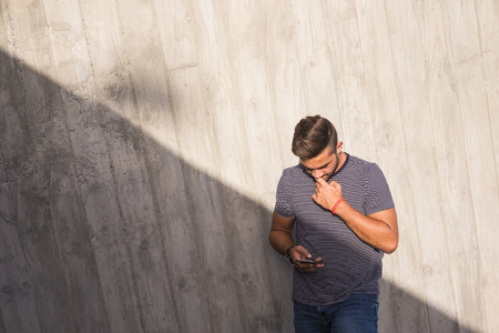 young caucasian teenager man use the phone to connect with friends and check emails and social media on internet. light and shadow composition in the urban city. wall backgroundの写真素材