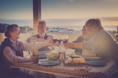 Group of cheerful caucasian adult senior people having fun together cheering and toasting with wine and food during outdoor dinner together in a terace with city view - vacation and leisure ativity conceptの写真素材