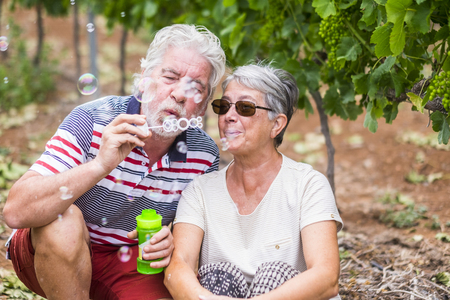 senior mature people have fun together in couple enjoying bubble soap - colors and people enjoying the playful lifestyle - caucasian adults in outdoor leisure activity - smile and cheerfulの写真素材