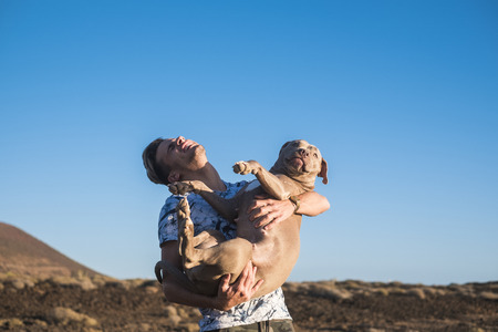 laughing a lot havinf fun in friendship blonde young man hugging and carrying his best friend puppy dog - forever together people and animals with love and cheerful leisure outdoor activityの写真素材