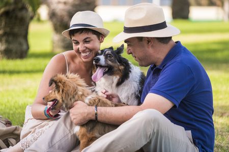 Happy couple animal dogs lover enjoy the leisure activity together in the outdoor park smiling and having fun with their two adorable lovely pets - caucasian people hve funの写真素材
