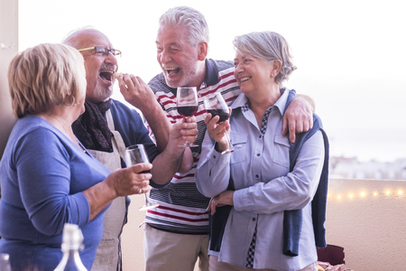 Group of matures adults people having fun together in friendship kidding and joking outdoor at home - eat and drink friends caucasian retired men and women with lot of laughs - cheerful lifestyleの写真素材